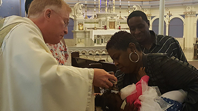 Fr. Bob Kelly, SVD baptises a baby at St Anselm's parish in Chicago, Illinois