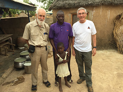 Fr. Fred Timp poses with two men and a small child in an African village