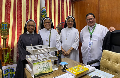 Fr. Ruel standing with three religious sisters in his university office