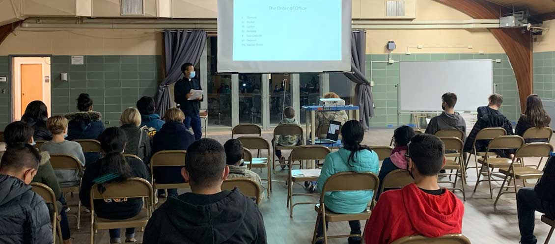 Frt. Boromeo Seo leads a class of teenagers who are sitting in folding chairs