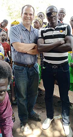 Two men standing side by side. One is smiling