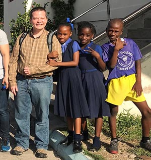 Caucasian man smiling next to three Jamaican school girls