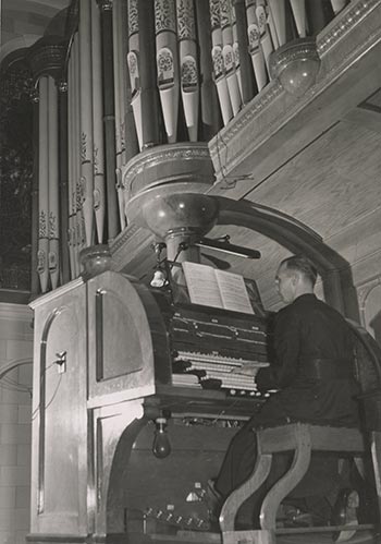 Historical photo of man playing a pipe organ in a church