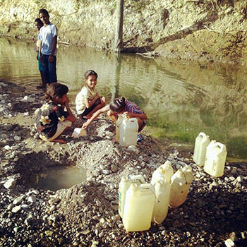 Children at the edge of a river filling plastic jugs with water