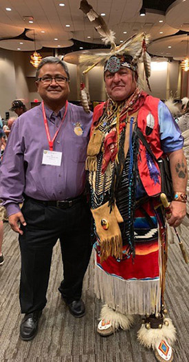 Man in purple shirt standing next to Native American man in full ceremonial dress