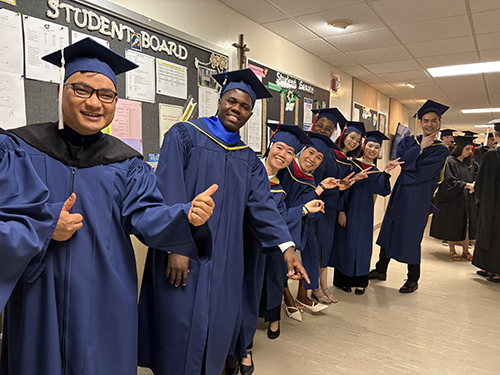 Graduates in blue robes flash a peace sign to the camera